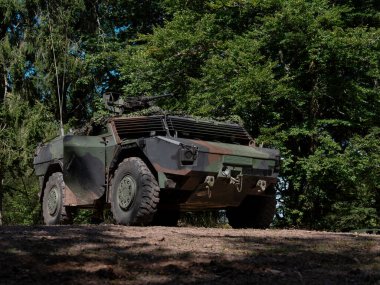 Taktik gizleme için ağaçların arasına yerleştirilmiş kamufle edilmiş askeri araç.