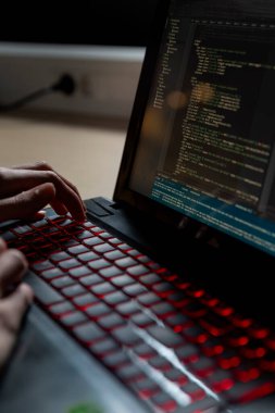 Ekranda gösterilen programlama koduyla birlikte kırmızı arka plan klavyesinde yazı yazan ellerin yakın plan görüntüsü