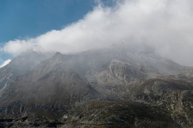 Bulutlarla kaplı dağ sırası dramatik zirvelerle atmosferik alp manzarası yaratıyor.
