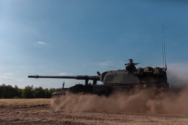 Açık mavi gökyüzü koşulları altında çalışan mürettebatlı, itici motorlu bir obüs.