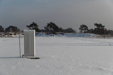 Beyaz radyatör karlı alana yerleştirilmiş bulutlu gökyüzü altında, gerçeküstü kavramsal sahne