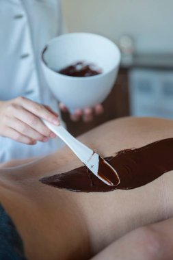 Sağlık seansı sırasında spatulayla çikolata vücut tedavisi uygulayan bir spa terapisti.