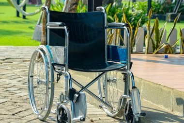 Boş, parlak gümüş ve siyah bir tekerlekli sandalye, arka planda bulanık yeşil çimlerin ve ağaçların bulunduğu tuğla bir yolda oturur ve sağlık ve maluliyet farkındalığı için uygun barışçıl ve ulaşılabilir bir ortam yaratır..