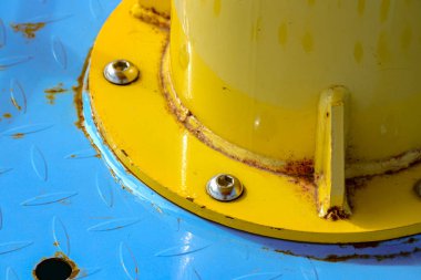 Mavi metal bir plakaya bağlanmış sarı boru tabanı kenarlarda biraz pas gösteriyor. Yapım ve üretim için uygun dokulu, endüstriyel ve yıpranmış bir his yaratıyor..