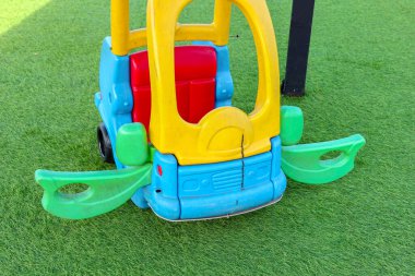 Parlak mavi ve sarı plastik oyuncak araba yemyeşil çimlerde oturur, eğlenceli ve eğlenceli bir atmosfer taşır, çocukların içeriği ve aile temalı reklamlar için uygundur.