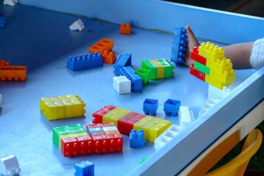 Çocuğun eli, mavi bir masanın üzerinde renkli plastik bloklarla çocuk ürünleri ve öğrenme materyalleri için ideal, eğlenceli ve eğitici bir sahne yaratırken görülüyor..