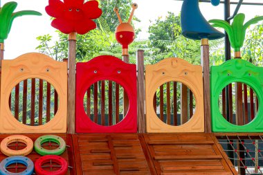 Ahşap güverteli renkli bir oyun alanı yapısı canlı kırmızı, sarı ve yeşil elementler içerir, eğlence tesisi veya çocuk tasarım projeleri için mükemmel bir ortam yaratır..