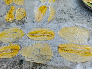 Sarı susuz muz dilimleri, dokulu gri bir yüzey üzerine parşömen kağıdının üzerine serilir. Bu da yemek pişirme ve sağlıklı beslenme içerikleri için soyut bir yemek hazırlama sahnesi yaratır..