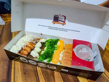 Etkili malzemelerle çeşitli suşi dürümleri açık bir kutuda sergileniyor, çeşitlilik gösteriliyor ve göz alıcı renkler ve dokularla çekici hale getiriliyor, yemek ve yemek servisi için mükemmel..