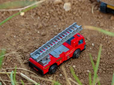 Küçük kırmızı oyuncak itfaiye aracı kahverengi topraklarda dinleniyor. Çocukların içeriği ve yaratıcı tasarımları için mükemmel, eğlenceli ve yaratıcı bir atmosfer yaratıyor..