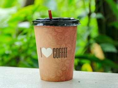 Kapaklı ve samanlı kahve fincanı, yeşil bir zemine karşı kahve çekirdeği desenli bir yüzey üzerinde oturur, rahatlatıcı ve davetkar bir ruh hali sunar, kafe veya içecekle ilgili içerik için mükemmeldir..