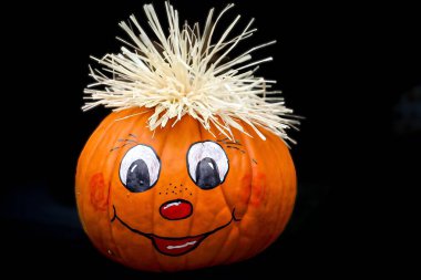 Canlı bir turuncu balkabağı el boyaması gülümseyen bir yüzle, büyük beyaz gözbebekleri, kırmızı yanakları ve küçük kırmızı bir burnu ve ağzı ile süslenir. Yüksek kalite fotoğraf