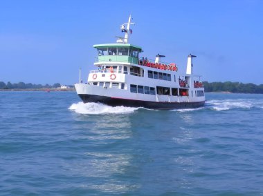 Bir yolcu feribotu berrak mavi gökyüzünün altında sakin sularda yol alır. Kırmızı aksanlı beyaz ve yeşil dış görünüşü canlı bir deniz manzarası yaratıyor. Seyahat, ulaşım ve deniz yaşam tarzı teması için ideal..