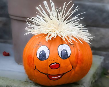 Painted pumpkin with cartoon face, straw hair, and cheerful expression. Set on stone steps outdoors, it captures festive autumn spirit, DIY creativity, and seasonal charm. Ideal for Halloween, harvest, or decorative themes.