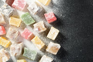 Farklı renkte ve tatlarda çeşitli Türk lokum şekerlerinin yukarıdan görünüşü, pudra şekeriyle kaplı, siyah bir mutfak tahtasına saçılmış. Kopyalama alanı olan renkli yiyecek arkaplanı.