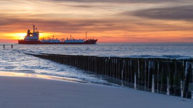 Sunset at the coast of Vlissingen Holland with the wooden poles clipart