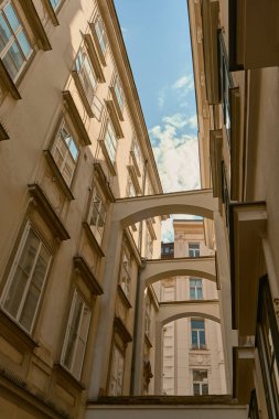 Güneşli tarihi cepheleri, binalar arasında kemerleri ve parlak mavi gökyüzü olan bir Viyana caddesinin uzak kenar manzarası klasik Avrupa kentsel cazibesini yakalıyor..