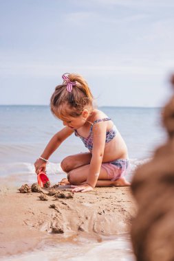 Küçük bir kız suyun hemen yanındaki kumda oynamaya odaklanmış. Sakin ve huzurlu bir kumsal anı..