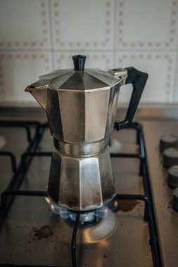 Metal moka demliği eski bir gaz ocağında kahve demliyor, İtalyan kahve kültürünün ve klasik mutfak cazibesinin özünü yakalıyor..