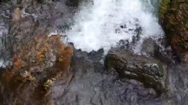 Ilımlı bir şelale akıntısı kayalık arazide yuvarlanır, sık bir ormanda zikzak çizer. Enerjik akış ve saf su doğanın dokunulmamış güzelliğini vurgular.