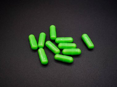 Yeşil kapsüller karanlık bir yüzeye dağılmış, pürüzsüz, parlak kaplamalarını sergiliyorlar. Bu yüksek çözünürlüklü görüntü vitaminleri, bitkisel takviyeleri veya sağlıkla ilgili içeriği desteklemek için mükemmeldir.