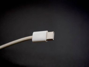 Temiz, karanlık bir yüzeye yerleştirilmiş beyaz USB-C şarj kablosunun yakın çekim görüntüsü. Görüntü, yükleme aksesuarının minimalist ve modern tasarımını vurgular