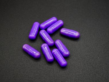 Siyah arka planda rastgele dizilmiş parlak mor kapsüller. Reklamlar, web siteleri veya ilaç tedavisi veya sağlıkla ilgili eğitim materyalleri için uygun görüntü
