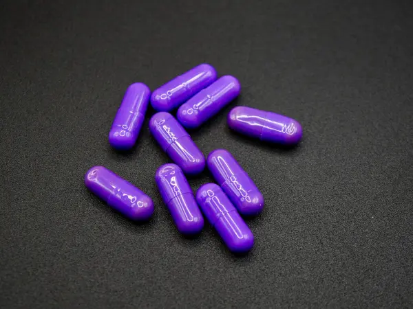 Siyah arka planda rastgele dizilmiş parlak mor kapsüller. Reklamlar, web siteleri veya ilaç tedavisi veya sağlıkla ilgili eğitim materyalleri için uygun görüntü