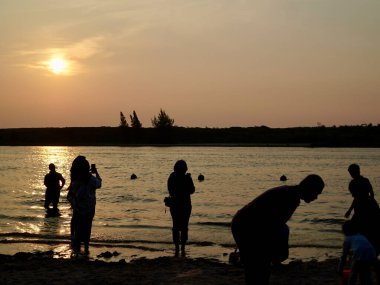 Cakarta, Endonezya - 12 Temmuz 2025: Bir grup insan, kıyı şeridinde sıcak, turuncu bir günbatımı gökyüzüne karşı siluet içinde yakalanarak, doğayla bir sakinlik, özgürlük ve bağlantı hissi uyandırdılar.