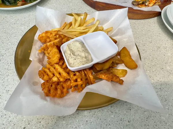 Yuvarlak altın bir tabakta servis edilen patates kızartmaları, patates kızartmaları ve waffle kızartmaları da dahil olmak üzere leziz bir çeşitlilik. Yemek kremalı bitki sosuyla tamamlanıyor.