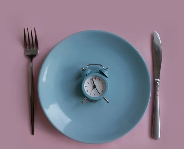 Alarm clock, plate, fork knife on a colored background