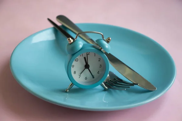 Alarm clock, plate, fork knife on a colored background