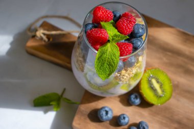 Yogurt, chia seeds, blueberries, strawberries, raspberries, mint, kiwi on a light background