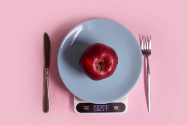 Apples, kitchen scales, plate, fork, knife on a colored background