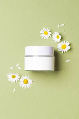 Yeşil arka planda papatya çiçekleri olan beyaz kozmetik kavanozu.