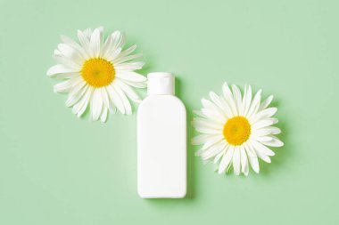 Yeşil arka planda iki papatya çiçekli beyaz kozmetik şişesi..