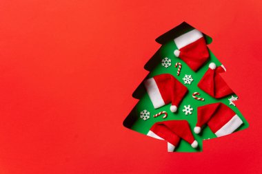 Noel ağacı kesimi, Noel Baba şapkaları, baston şekerler ve kırmızı şenlik arka planında kar taneleri.