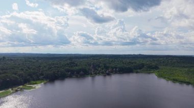 Bereketli yağmur ormanları, sakin Amazon gölüne hava perspektifinden yayılıyor. Yumuşak beyaz bulutların altındaki sakin suyu yansıtan yeşil bir tepe örtüsü..