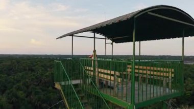 Sarışın kadın gezgin gözlem kulesinin tepesinde duruyor, altın saat boyunca yemyeşil Amazon yağmur ormanlarına bakıyor, yoğun yeşil gölgelik manzarasını süpürüyor..