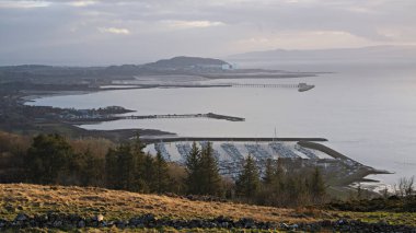 Haylie Brae bakış açısı, işletim sistemi haritası hakemi NS 214 585. Largs, Ayrshire, İskoçya. 1 Mart 2025. Largs marinasının, Fairlie rıhtımının ve Hunterston Elektrik Santralinin akşam ışığı manzarası. 