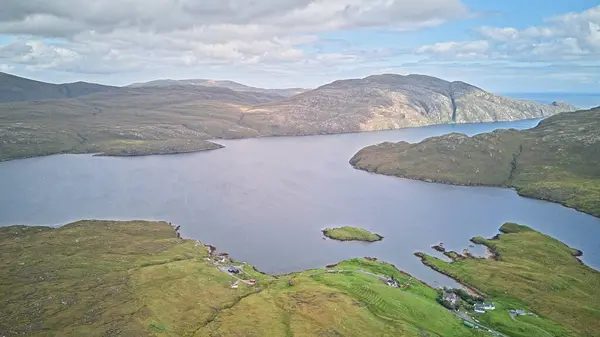 Etrafı yemyeşil tepelerle çevrili sakin bir göl ve sudaki küçük bir adayla bulutlu bir gökyüzü..