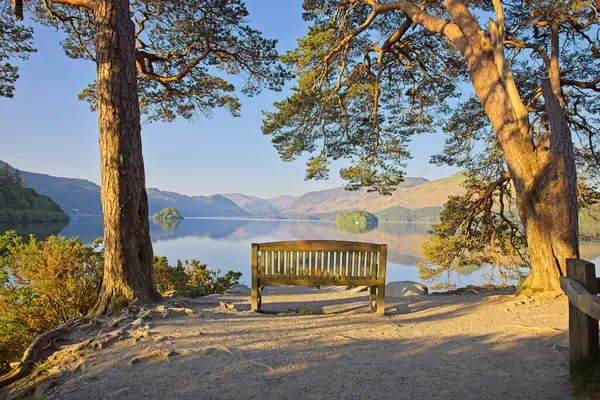 İngiltere Gölü 'nde, dağlarla çevrili, ağaçlarla çerçevelenmiş ve ahşap bir bankın yer aldığı Derwen Suyu Keşiş Kayalıkları' nın sakin bir manzarası..