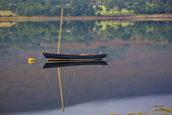 Bir yelkenli sakin bir gölde huzur içinde yüzer. Yansıması sudaki yansıması yemyeşil ağaçlardan ve dingin doğal güzellikten oluşan bir zemin ile aynalıdır..