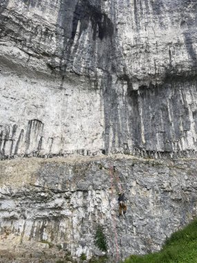 Malham, bir kaya tırmanıcısı dik bir yamaçtan tırmanır, ipleri güvenlik için kullanır. Yükselen kaya oluşumu yeryüzüne hakim..