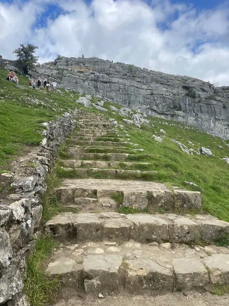 Malham, Stone parçalı bulutlu bir günde, kayalık bir dağın zirvesine çıkan çimenli bir yamaçtan yükseliyor..