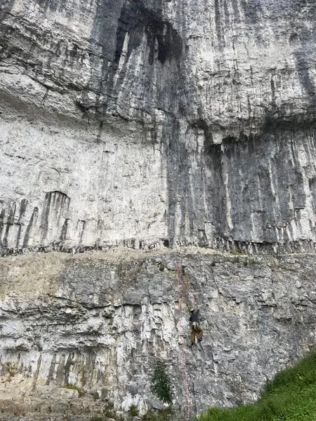 Malham, bir kaya tırmanıcısı dik bir yamaçtan tırmanır, ipleri güvenlik için kullanır. Yükselen kaya oluşumu yeryüzüne hakim..