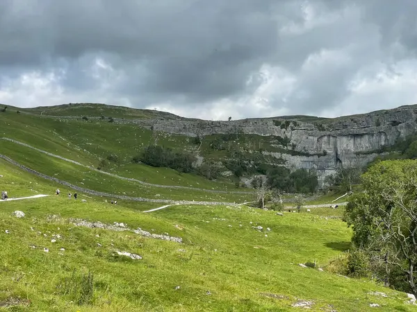 Malham, yemyeşil bir vadinin manzaralı manzarası. Yürüyen patikalar bulutlu bir gökyüzünün altında dramatik bir uçuruma doğru gidiyor..