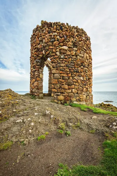 Okyanusa bakan bir uçurumun üzerinde, bulutlu bir gökyüzünün altında güneş ışığıyla yıkanmış bir taş kule duruyor. İskoçya 'daki Kadın Kulesi.