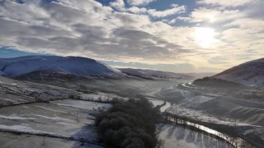 Karla kaplı tepelerle kaplı güzel bir kış manzarası ve bulutlu bir gökyüzünün altında biraz güneş ışığı olan dolambaçlı bir nehir. Howgill Şelaleleri 'nin ve M6 otoyolunun üzerinde beyaz karla kaplı bir şekilde kış sabahının şafağına doğru uçuyor.. 