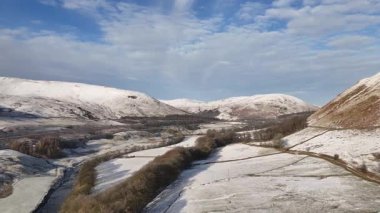 Karla kaplı tepelerle, bir vadiyle ve güneşli bir günde bulutlu mavi gökyüzüyle nefes kesici bir kış manzarası. Howgill Şelaleleri ve M6 otoyolunun üzerinde beyaz karla kaplı bir şekilde kış sabahının doğuşuna doğru uçuyor. Yorkshire Dale İngiltere.